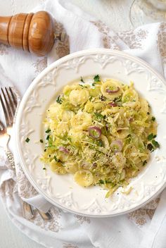 a white plate topped with pasta and veggies on top of a table next to silverware