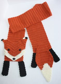 an orange scarf with a black and white fox design on it, sitting next to a red knitted scarf