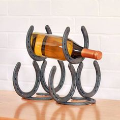 a wine bottle holder made out of horseshoes on a table with a brick wall in the background