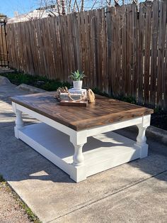 a white coffee table sitting on top of a cement ground next to a wooden fence