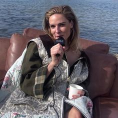 a woman sitting on top of a brown couch next to a lake holding a cup