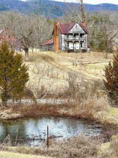 an old abandoned house in the middle of nowhere with a pond and trees around it