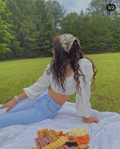 a woman sitting on top of a blanket next to a plate of food