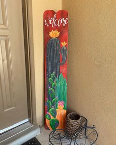 a welcome sign on the side of a door next to a potted cactus and wicker basket