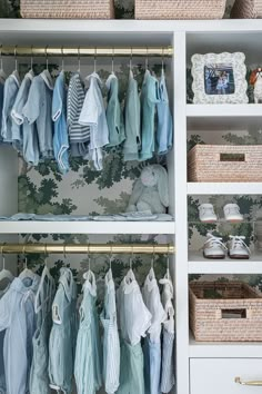 an organized closet with baby clothes hanging on the shelves and wicker baskets under them