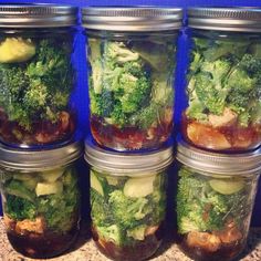 four mason jars filled with different types of vegetables and meats, sitting on a granite countertop