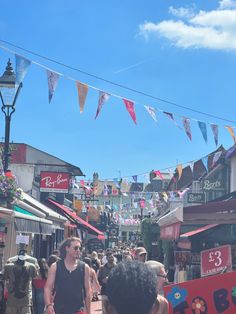 people walking down a crowded street with bunting and banners above them on a sunny day