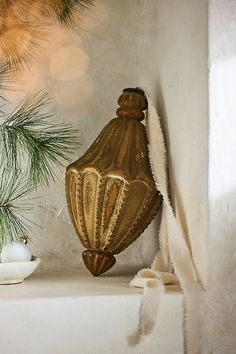 a gold vase sitting on top of a white shelf next to a pine tree branch