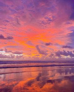 the sky is reflected in the wet sand on the beach as the sun goes down