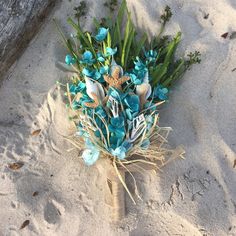 a bouquet of blue flowers on the sand at the beach with seaweed and starfish