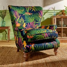 an upholstered chair with tropical print on the back and arms in front of a green wall