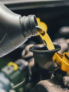 the yellow liquid is being poured into the black cup on top of the car's engine