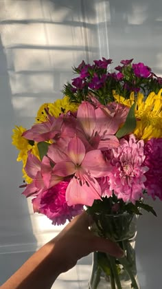 a vase filled with lots of colorful flowers on top of a table next to a person's hand