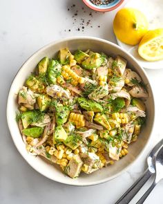 a white bowl filled with corn and meat next to two lemons on the side