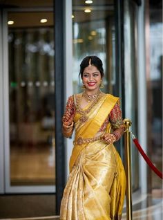 a woman in a yellow sari holding a gold pole and smiling at the camera