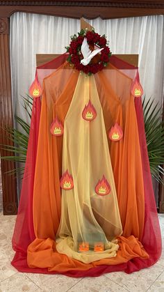 an altar decorated with orange and red cloths, candles and flowers on top of it