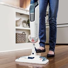 a woman is using a vacuum to clean the floor in her house with blue jeans and black slippers