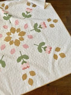 a white quilt with pink and green flowers on it sitting on top of a wooden floor