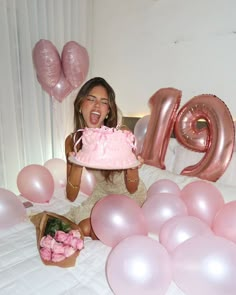 a woman holding a pink cake in front of balloons and the word mom spelled out