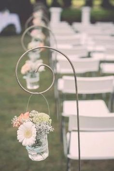 rows of white chairs are lined up with flowers in vases hanging from the back