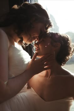 two women in white dresses standing next to each other near a window with sunlight streaming through the windows