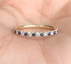 a woman's hand holding a gold ring with blue and white stones