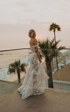 a woman standing on top of a roof next to the ocean wearing a wedding dress