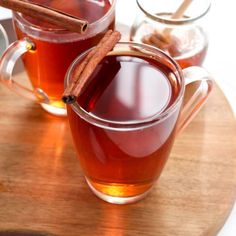 two mugs filled with cinnamon tea on top of a wooden cutting board