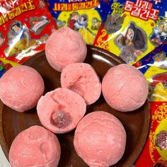 five pink donuts in a wooden bowl on a table with various candy bags behind them