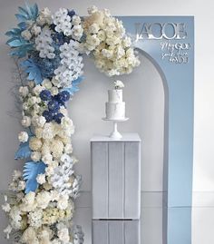 a white and blue wedding cake with flowers on it next to a tall arch that reads lace mirror photography