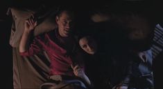 a man and woman laying on top of a bed in the dark with their arms around each other