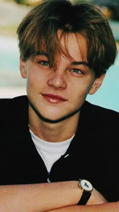 a young man with his arms crossed looking at the camera while wearing a watch on his wrist