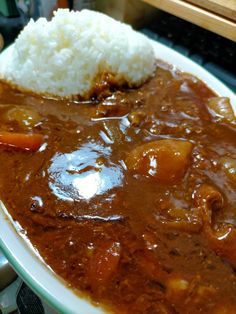 a white plate topped with meat and gravy next to rice on top of a table