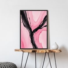 a pink and black painting on a white wall next to a table with a vase