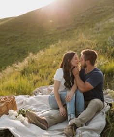 a man and woman sitting on a blanket in the grass