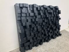 a large black piece of art sitting on top of a cement floor next to a wall