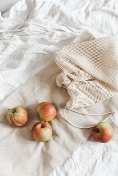 four apples sitting on top of a bed next to a drawstring bag and white linen