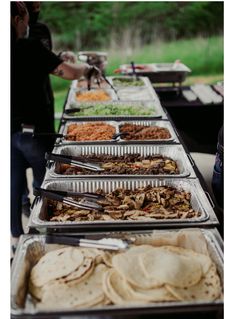 several trays of food are lined up on a table with people in the background