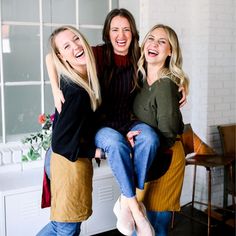 three women laughing and sitting on a stool