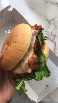 a hand holding a chicken sandwich with lettuce and tomato on it in a box