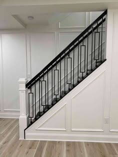 an empty room with white walls and black railings on the bottom floor, next to a stair case