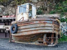 an old rusted boat sitting on top of a pile of junk next to a mountain