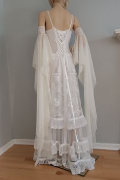 the back of a woman's white wedding dress with sheer sleeves and ruffles