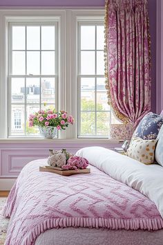 a bedroom with purple walls and pink bedding, flowers in vases on the window sill