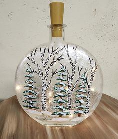 a glass bottle with trees in it on top of a wooden table next to a wall