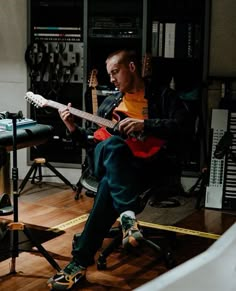 a man sitting in a chair playing an electric guitar with tape on the floor next to him