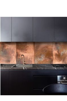 a black kitchen with copper backsplash and marble counter tops in an industrial style