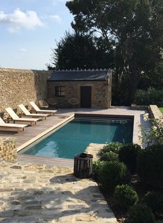 an empty swimming pool with chaise lounges next to it and a stone wall