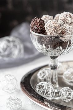 a glass bowl filled with chocolate balls on top of a metal tray next to silver ornaments