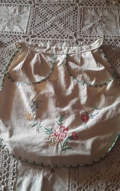 a white skirt with flowers on it laying on a lace doily covered tablecloth